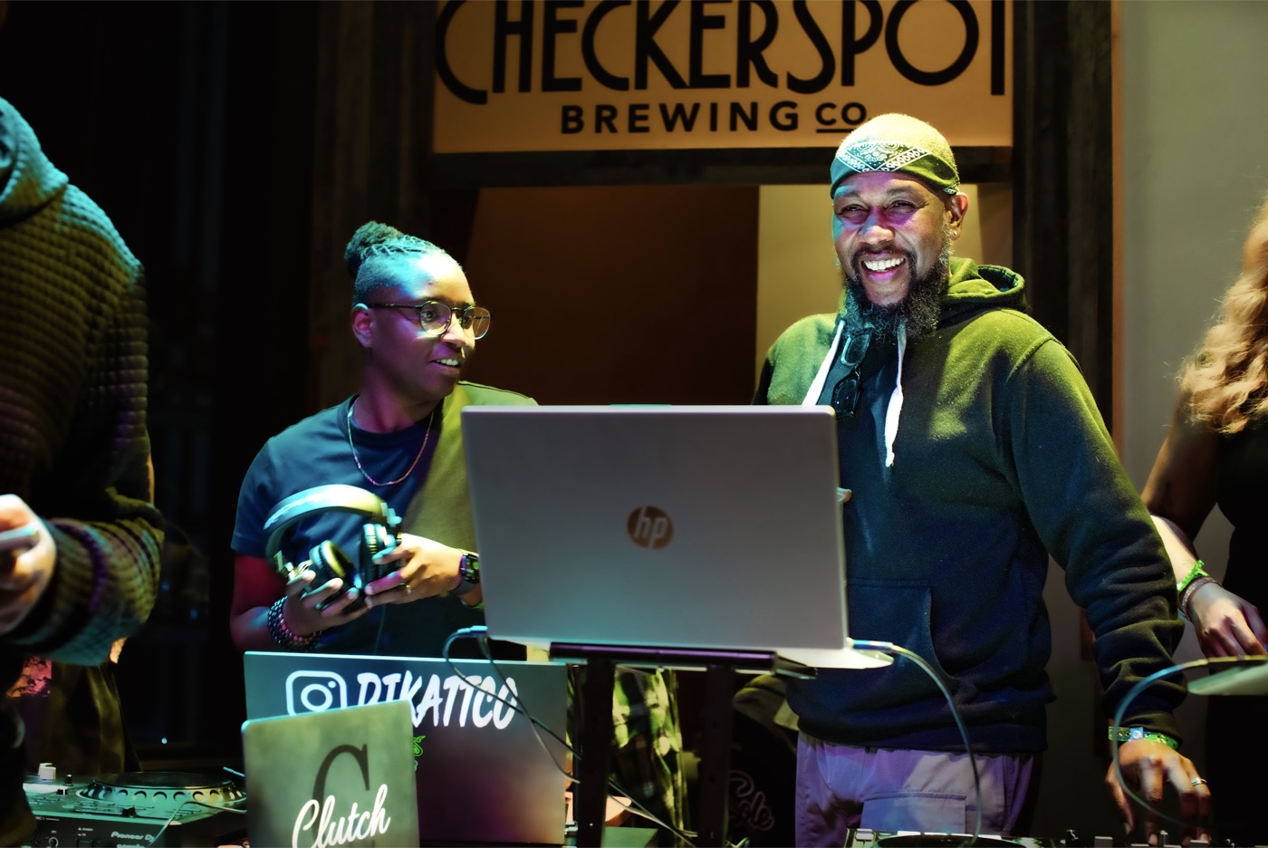 DJs spinning in front of the Checkerspot sign