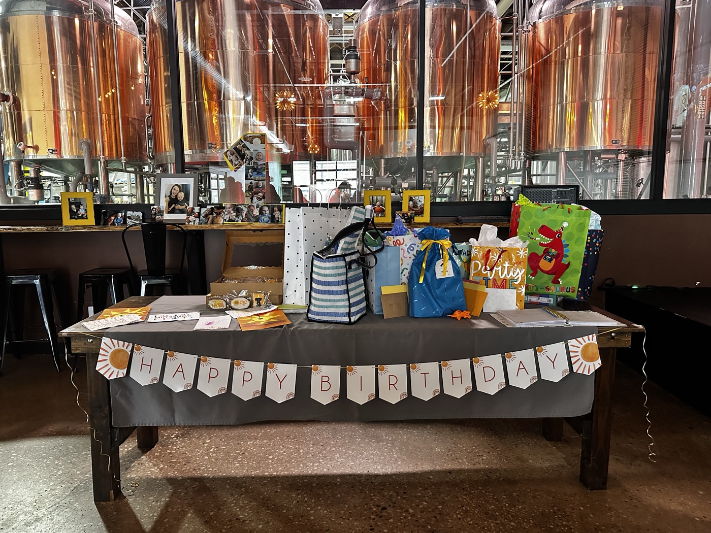A Happy Birthday banner and gift table in front of the copper brewhouse tanks